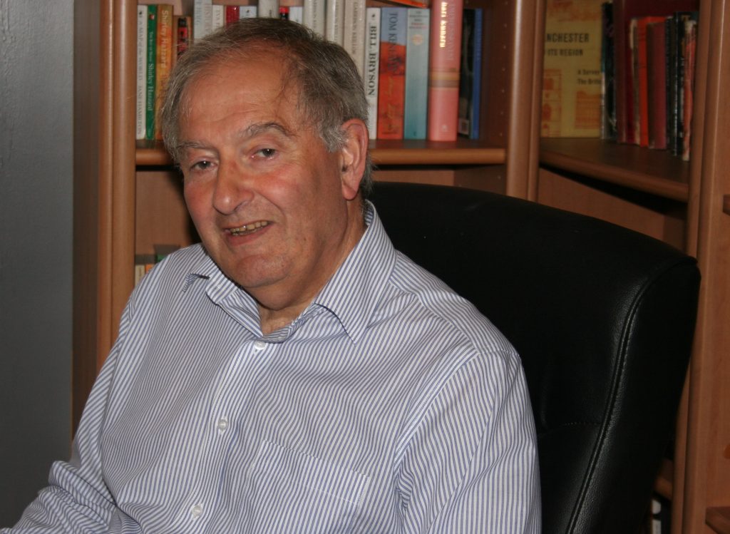 Prof Alan Bowman's profile photo. Prof Bowman wears a white shirt and is sitting in front of a bookcase.