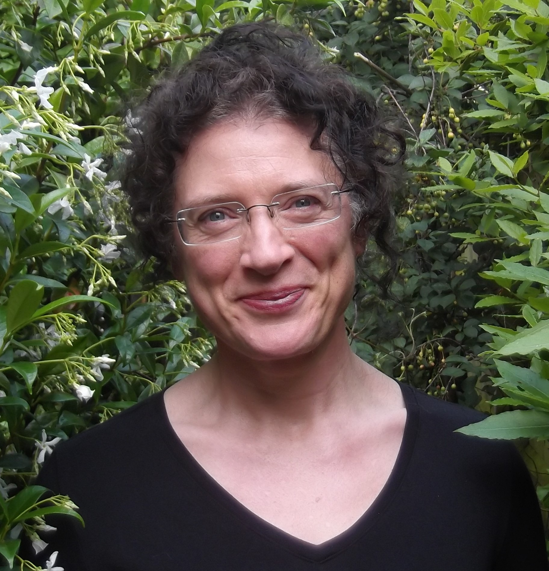 Amanda Holton profile photo. Amanda is pictured smiling and standing outside next to a large Jasmine plant