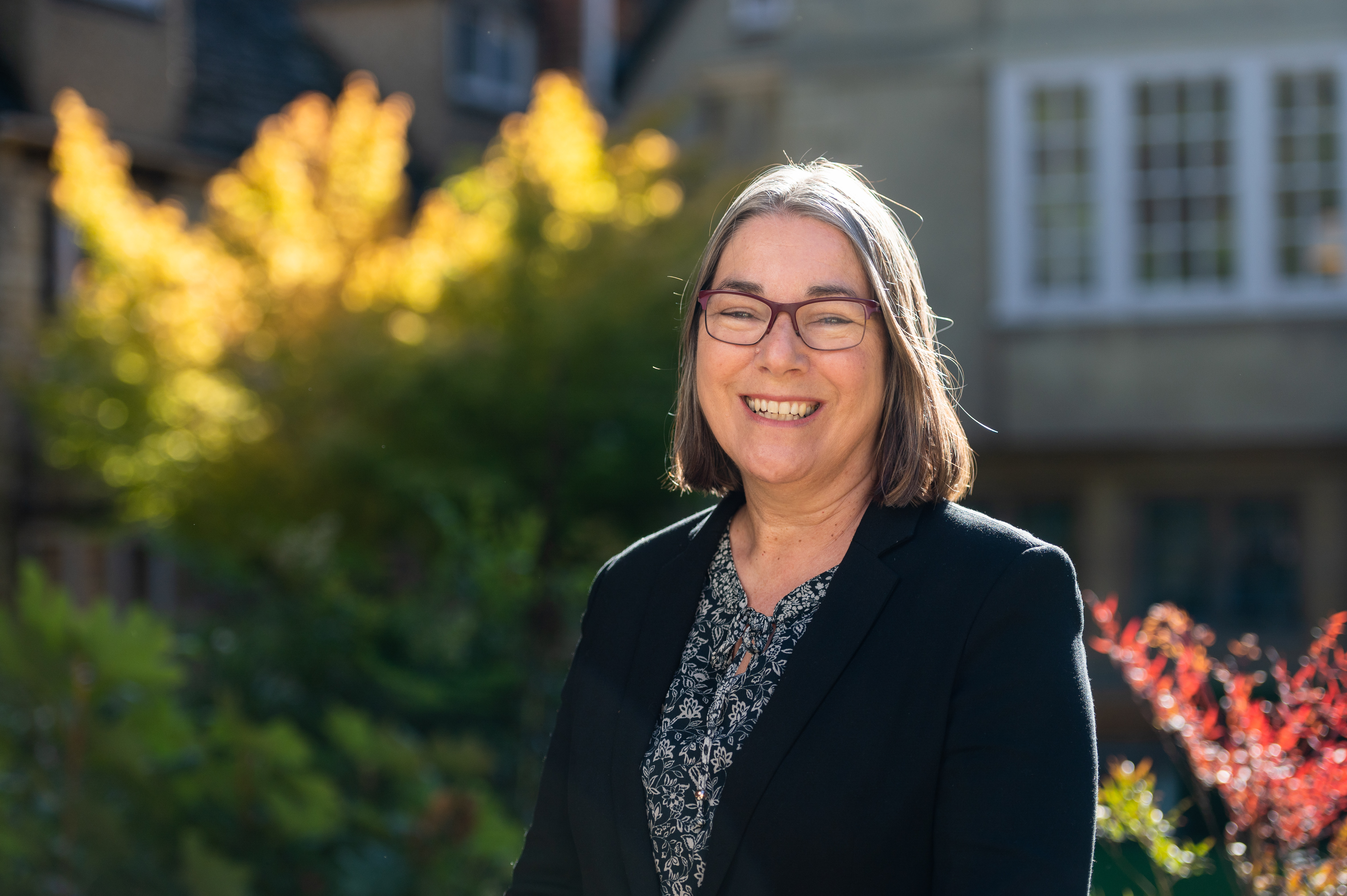 Catherine House's profile photo: Catherine wears a dark jacket and stands in front of an autumnal tree