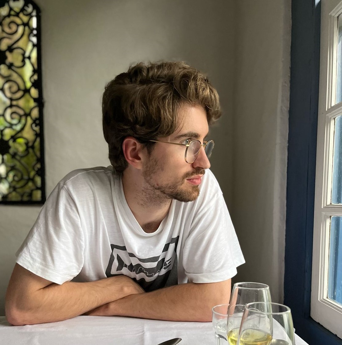 Joseph Hankinson profile photo. Joe is sitting at a table looking out the window to the right of the image. He is wearing a white t-shirt.