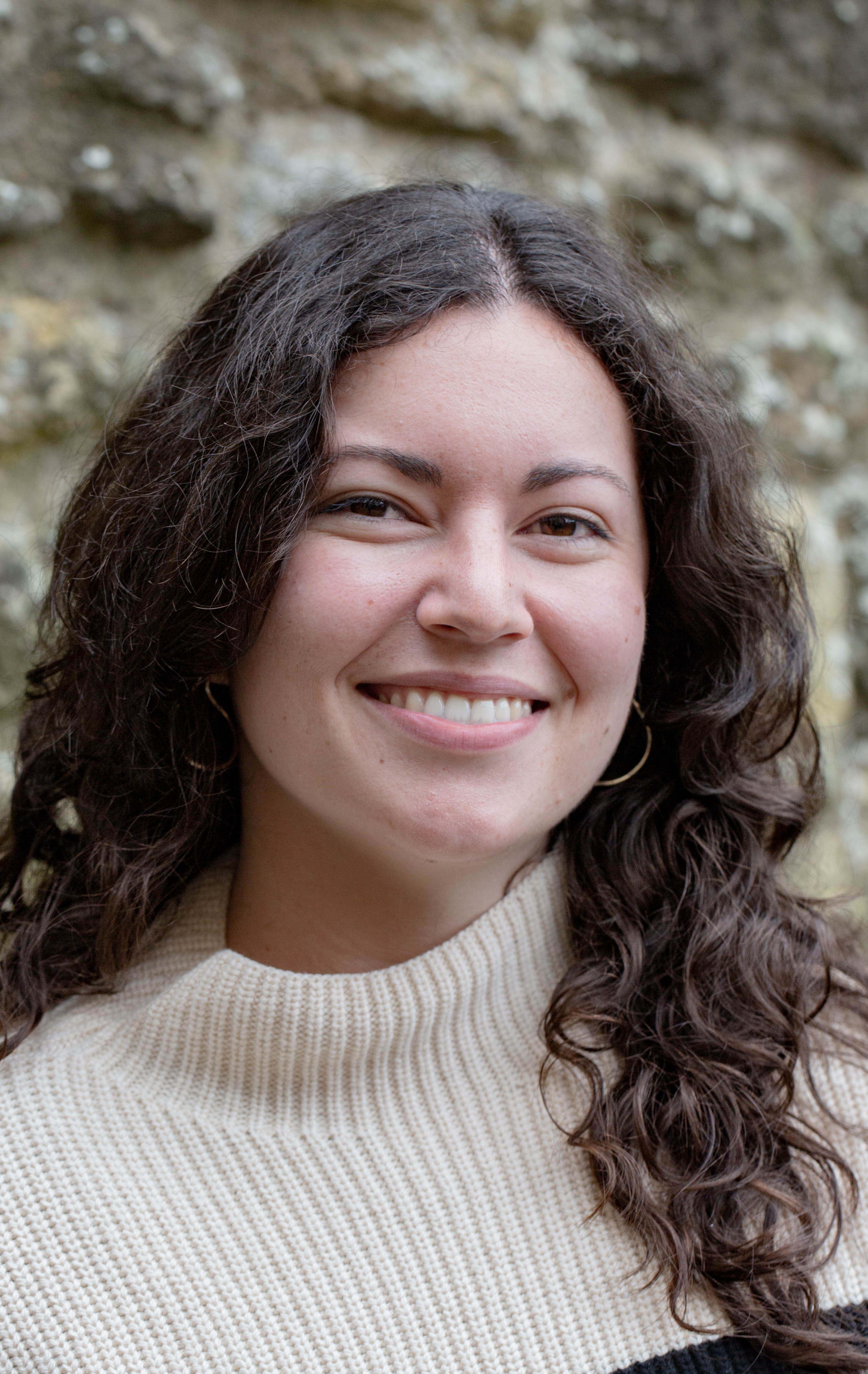 Sophie Elliott's profile photo. She is wearing a cream jumper and standing in front of a stone wall