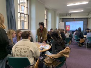 student outreach activities taking place with students around tables in a lecture room at Queen's