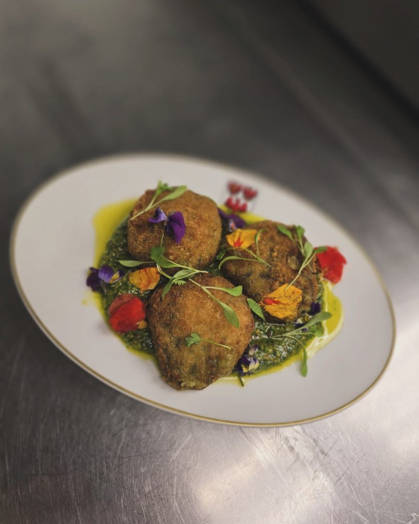 Rocket Croquette on a Queens-branded plate garnished with edible flowers