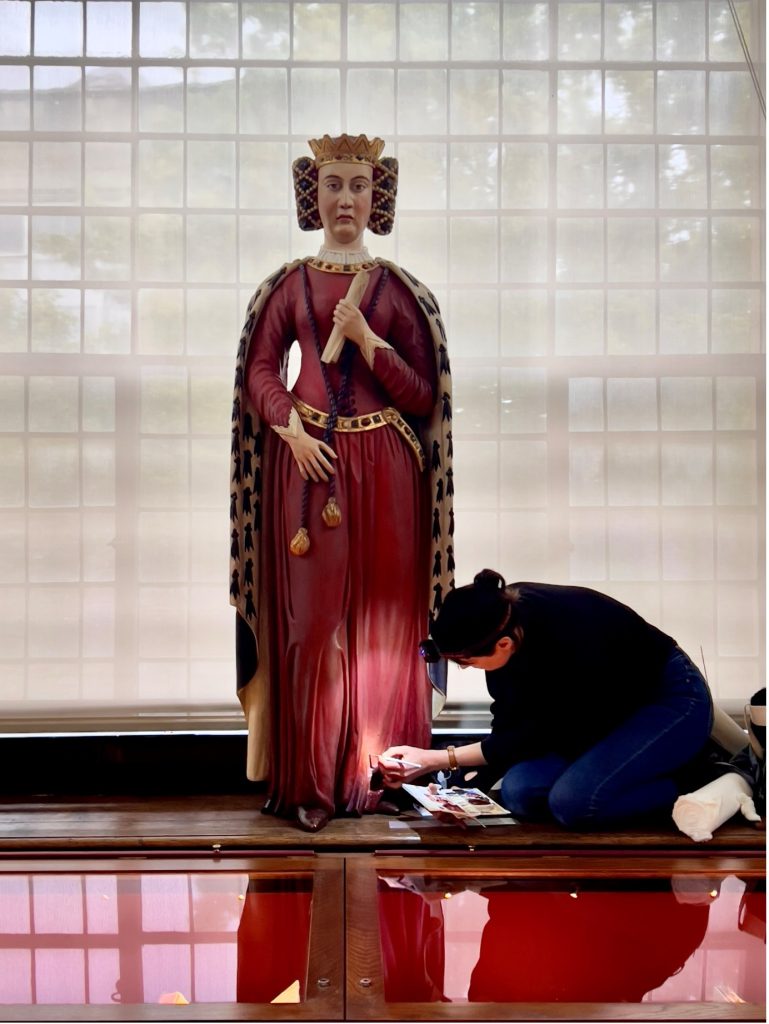 The statue of Queen Philippa in the Upper Library with someone kneeling at her feet and cleaning the paintwork