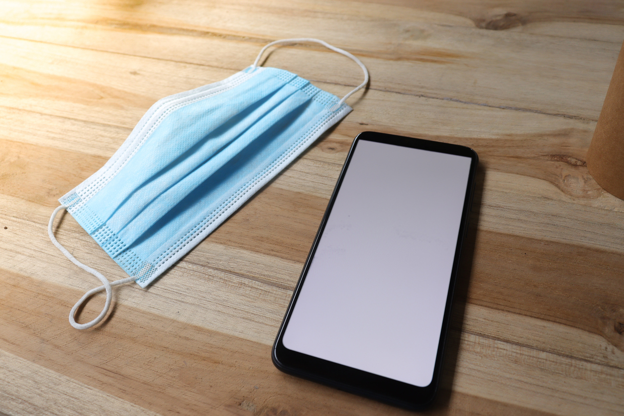 Top view of blank screen mobile phone and medical mask on wooden table