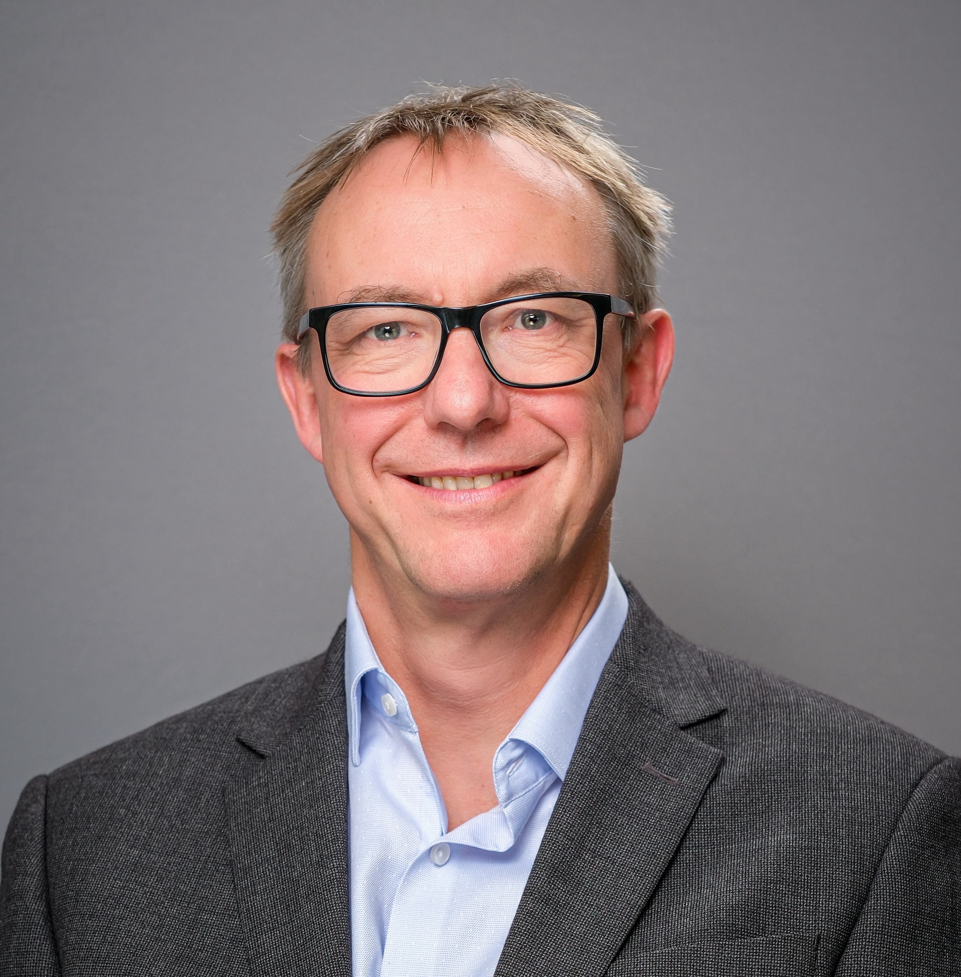 A profile photo of Paul Johnson wearing a grey suit jacket and a light blue shirt