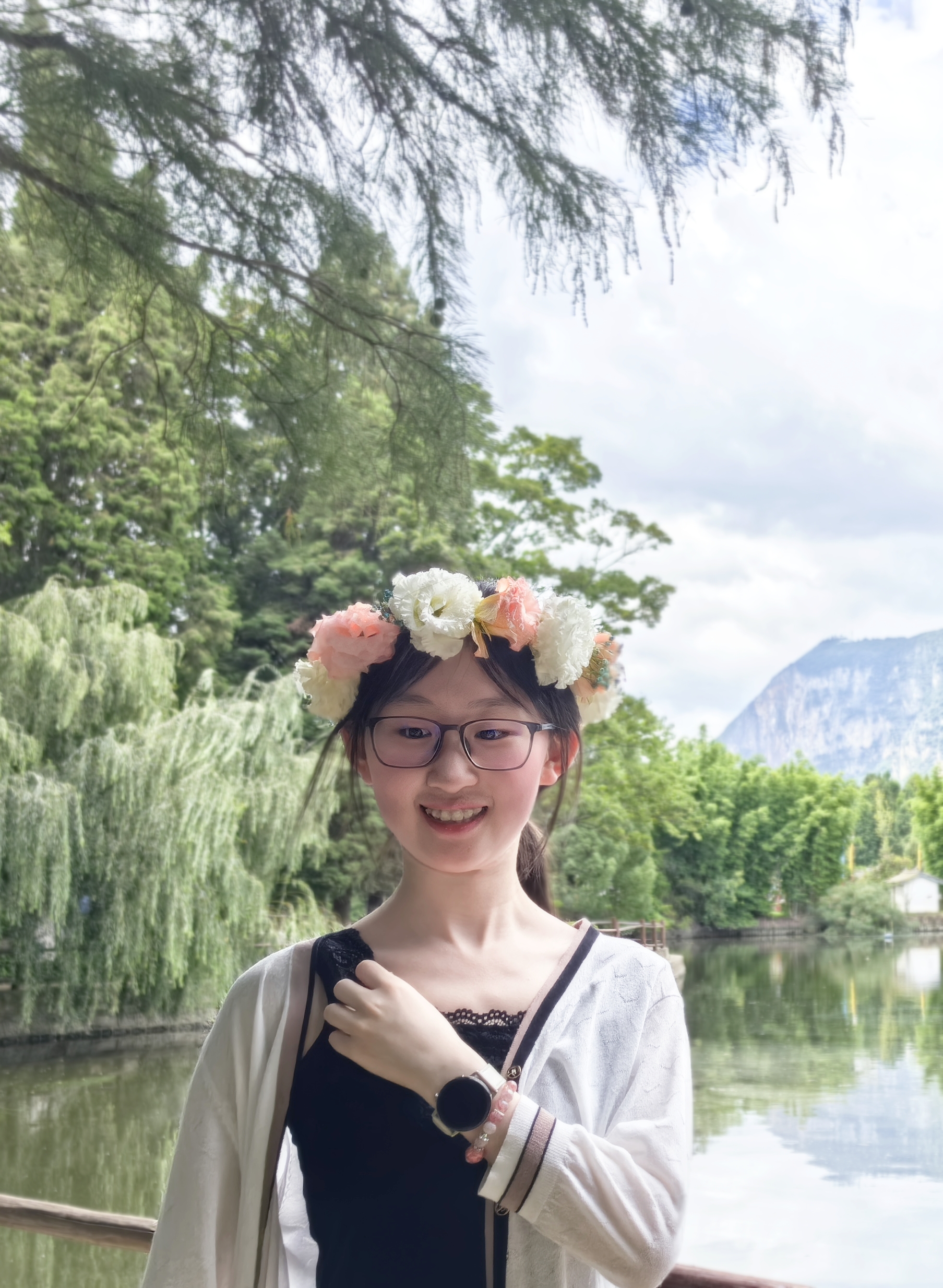 Xinyi profile photo. She wears a headband with flowers and there are trees, water and mountains in the background.