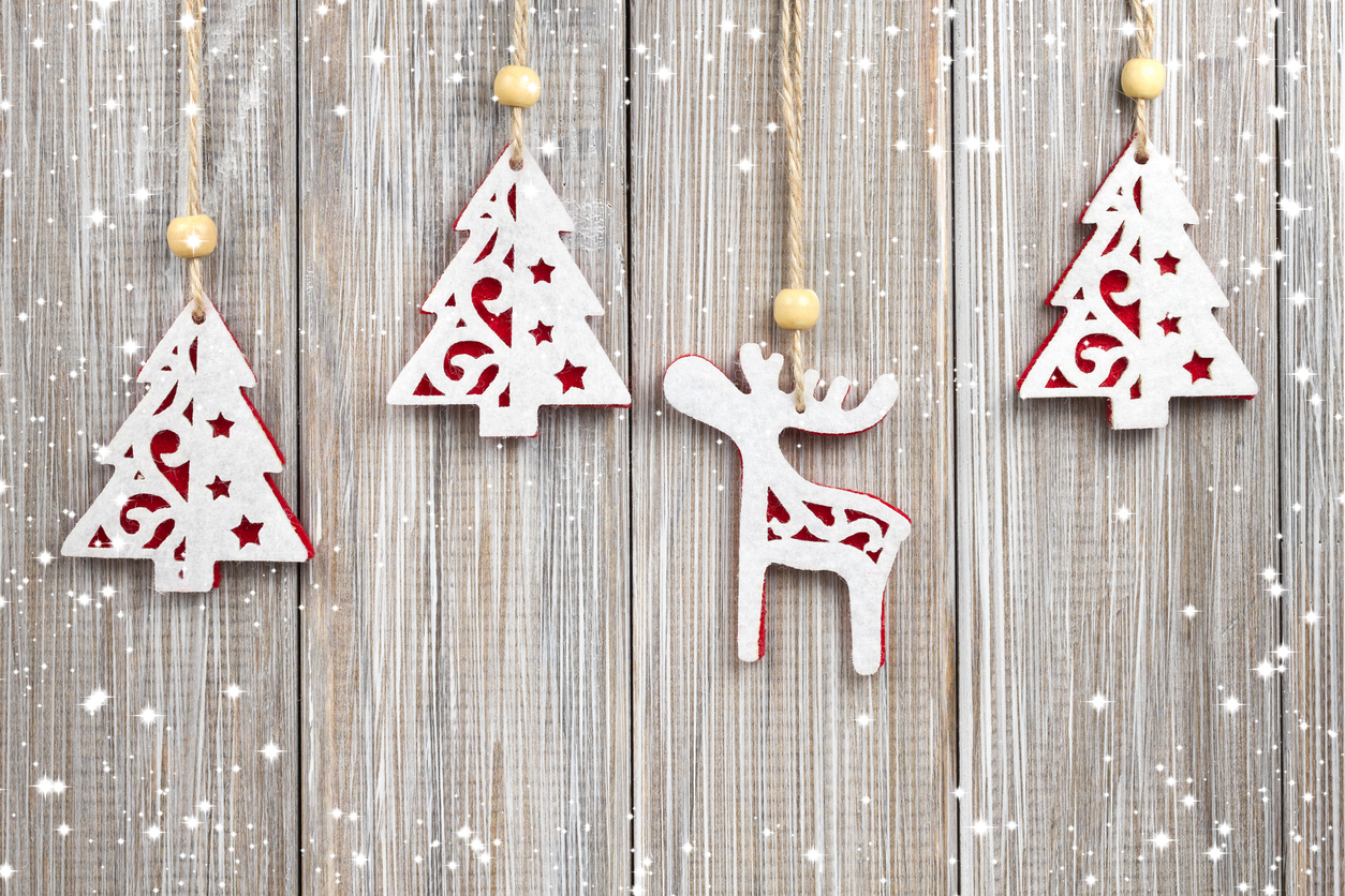 Hanging wooden Christmas decorations: three Christmas trees and one reindeer against a Scandi-inspired light wood background