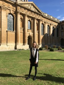 Phoebe's profile photo: she is standing in Front Quad wearing subfusc and holding her mortarboard