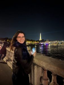 Victoria's profile photo: she stands on the banks of the Seine at nighttime with the Eiffel Tower illuminated in the background