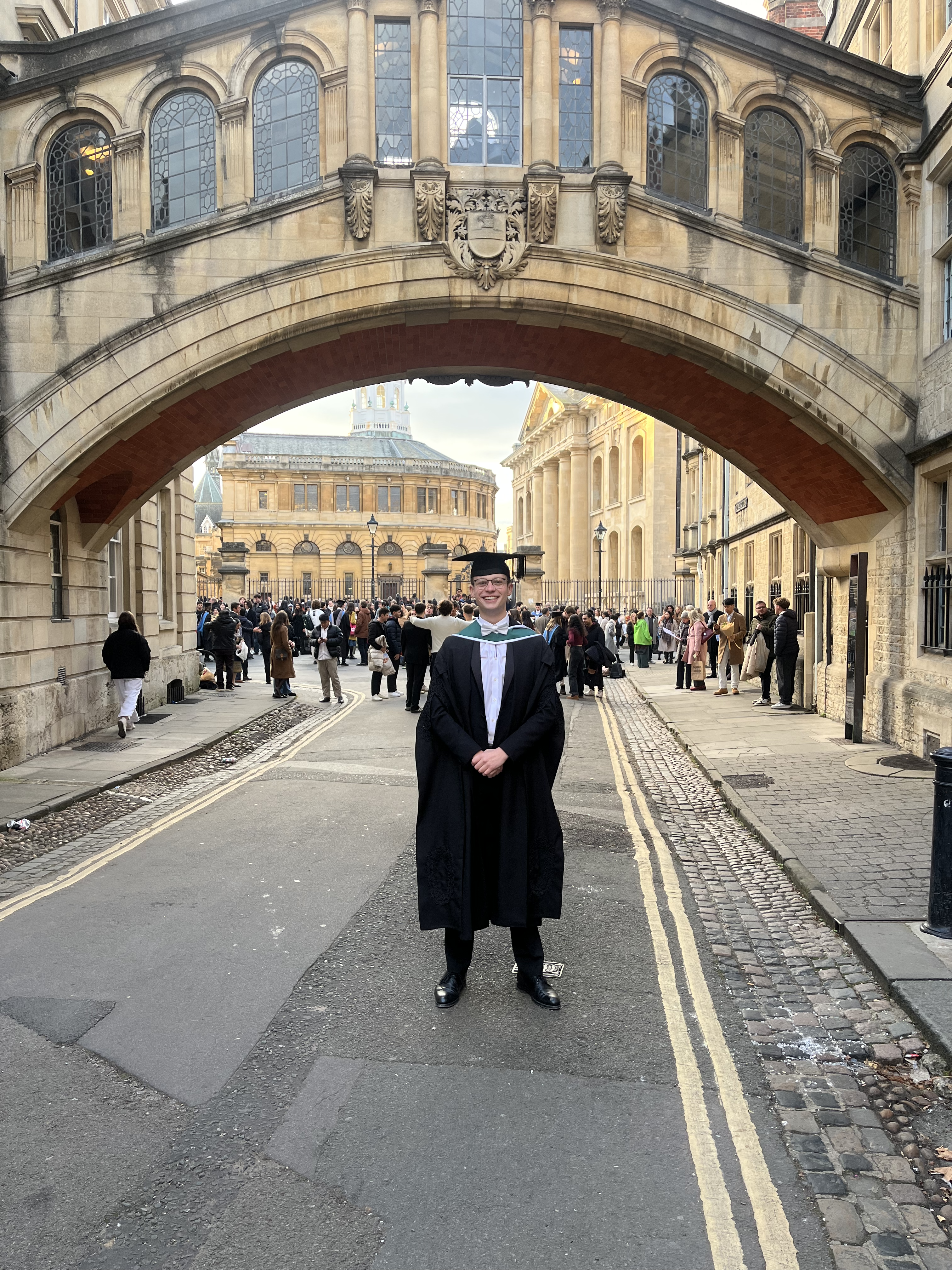 Kyle's profile photo. He is dressed in subfusc on graduation day standing underneath Oxford's Bridge of Sighs